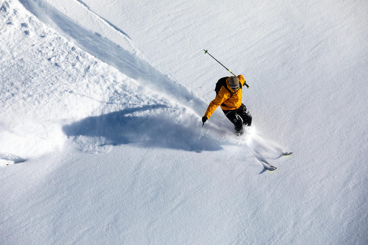 Skier and snowboarder riding on soft spring snow in May with mixed conditions of slush and refrozen patches on a mountain slope.